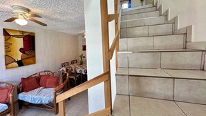 Eine Treppe mit Holzwerteln, ein Essbereich mit Stühlen und einem Tisch sowie ein Deckenventilator.