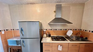 Eine Küche mit einem Zweitür-Kühlschrank, einem Gasherd, Holzschränken und einer gefliesten Spritzwand.