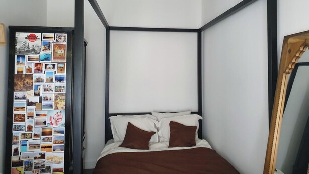 Een enkel bed met een zwart metalen frame, wit beddengoed en bruine kussens.