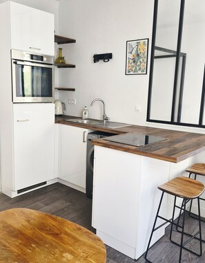A modern kitchen with white cabinetry, a built-in oven, a dishwasher, and a wooden island with bar stools. - Apartment in Buttes-Chaumont with courtyard (Paris)