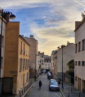 A narrow street lined with buildings, a parked car, and a person walking. - Apartment in Buttes-Chaumont with courtyard (Paris)