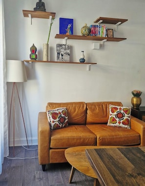A living room with a brown leather sofa, two decorative pillows, a floor lamp, and shelves with books and decorative items. - Apartment in Buttes-Chaumont with courtyard (Paris)