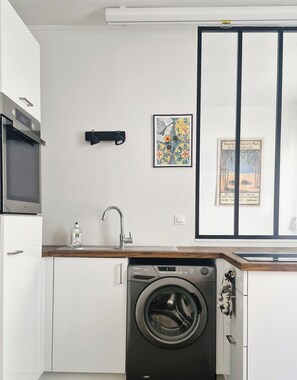 A compact kitchen with a washing machine, a microwave, and a sink. - Apartment in Buttes-Chaumont with courtyard (Paris)