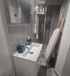 Ein Badezimmer mit weißem Waschbecken, einem Spiegel, einem Handtuchhalter und einer Duschkabine.
