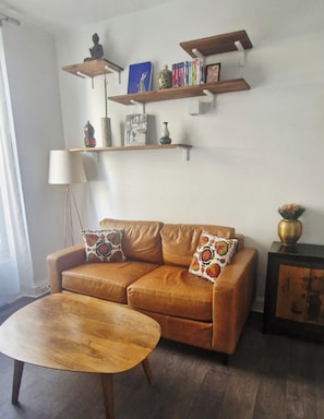 A living room with a brown leather sofa, two patterned throw pillows, a wooden coffee table, and a floor lamp. - Apartment in Buttes-Chaumont with courtyard (Paris)