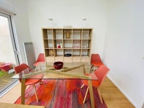 Un coin repas avec une table en verre, des chaises rouges, une bibliothèque et un tapis rouge.