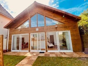 Une maison moderne avec un toit en pente, de grandes portes vitrées et une terrasse en bois.