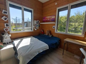 A wooden-paneled room with a bed, a desk, and two windows. - Wooden house with a large deck and a 5-person hot tub, not overlooked (Nivillac)