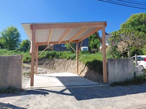A wooden structure with a roof, possibly a covered parking area or a small pavilion, surrounded by a concrete wall and a dirt path. - Wooden house with a large deck and a 5-person hot tub, not overlooked (Nivillac)