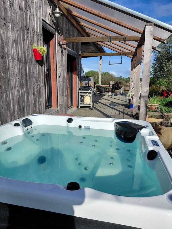 A hot tub in a wooden outdoor area with a pergola overhead. - Wooden house with a large deck and a 5-person hot tub, not overlooked (Nivillac)