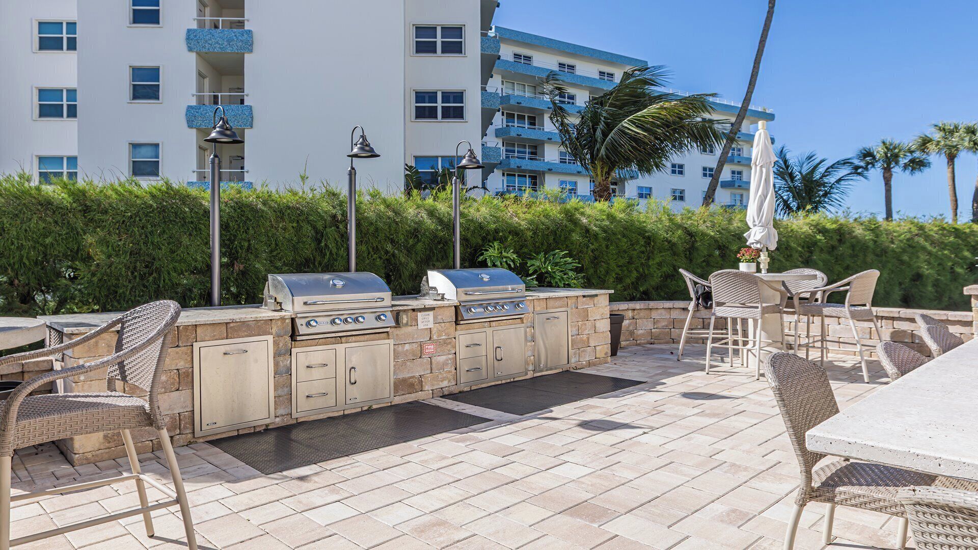 An outdoor patio with a grill, wicker chairs, and a view of a multi-story building.