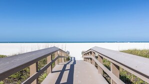 Un paseo marítimo de madera que lleva a una playa, con cielos despejados.
