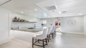 Una cocina moderna con encimera de mármol, taburetes de bar blancos y un gran reloj de pared.