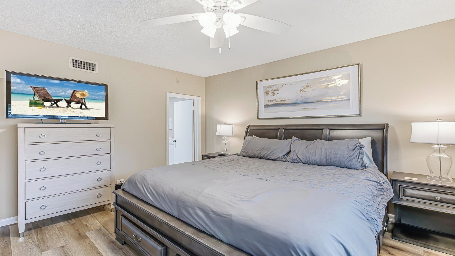 A bedroom with a bed, a dresser, a ceiling fan, a television, and a framed picture on the wall.
