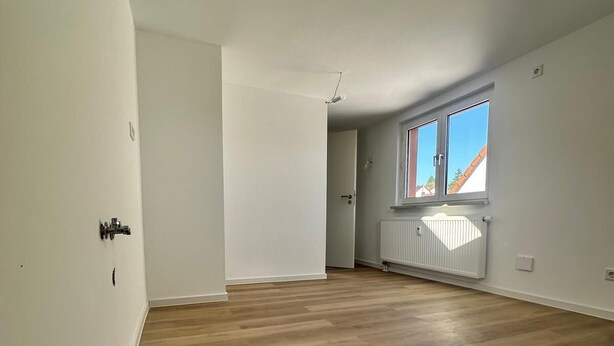 A spacious room with a wooden floor, white walls, and a window with a view of a building.