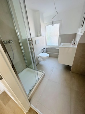 Ein Badezimmer mit Duschkabine, Toilette, Waschbecken und Fenster.