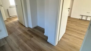 A corridor with wooden flooring, white walls, and a radiator.