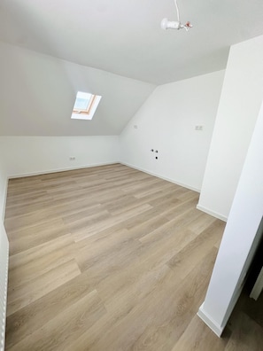 Ein geräumiges Dachzimmer mit schrägen Wänden, einem Oberlicht und Holzboden.