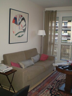 A living room with a beige sofa, a patterned rug, a lamp, and a window with curtains. - Boulogne (92) 10 min on Line 10 to Pont de Saint Cloud; easy access from the A10; 40 m² (Boulogne-Billancourt)