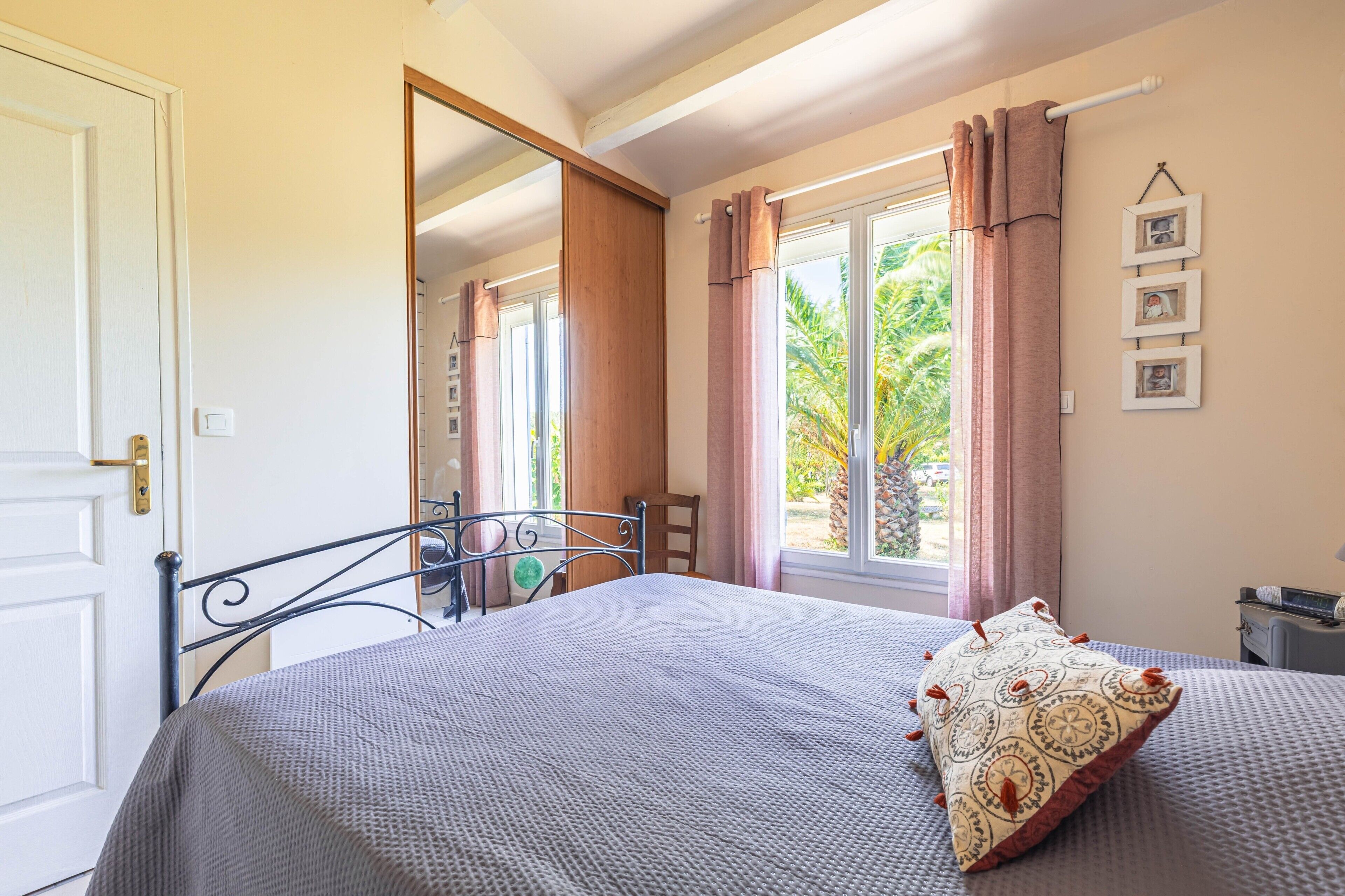 Une chambre à coucher avec un lit, une fenêtre avec des rideaux, une chaise, une table de chevet et une étagère murale décorée de tableaux.