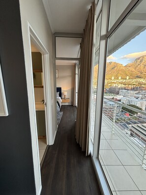 Un pasillo estrecho con vistas a un paisaje urbano y montañas a través de amplias ventanas.