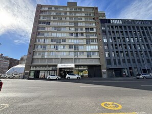 Un edificio de varios pisos con un cartel que dice 'PERSPECTIVES 37', indicando que es un hotel. Hay coches aparcados en la calle y un símbolo circular amarillo en la carretera.