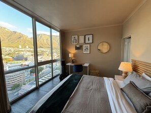 Una habitación de hotel con un ventanal grande, una cama, un escritorio y una silla.