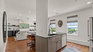 Een moderne keuken met een centraal eiland, een zithoek met een witte bank en uitzicht op groen.