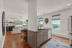 Eine moderne Küche mit einer zentralen Kochinsel, ein Essbereich mit einem weißen Sofa und Blick auf Grünflächen.