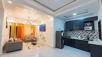 Una sala de estar moderna con un sofá, un televisor y una zona de cocina con refrigerador y salpicadero de azulejos.