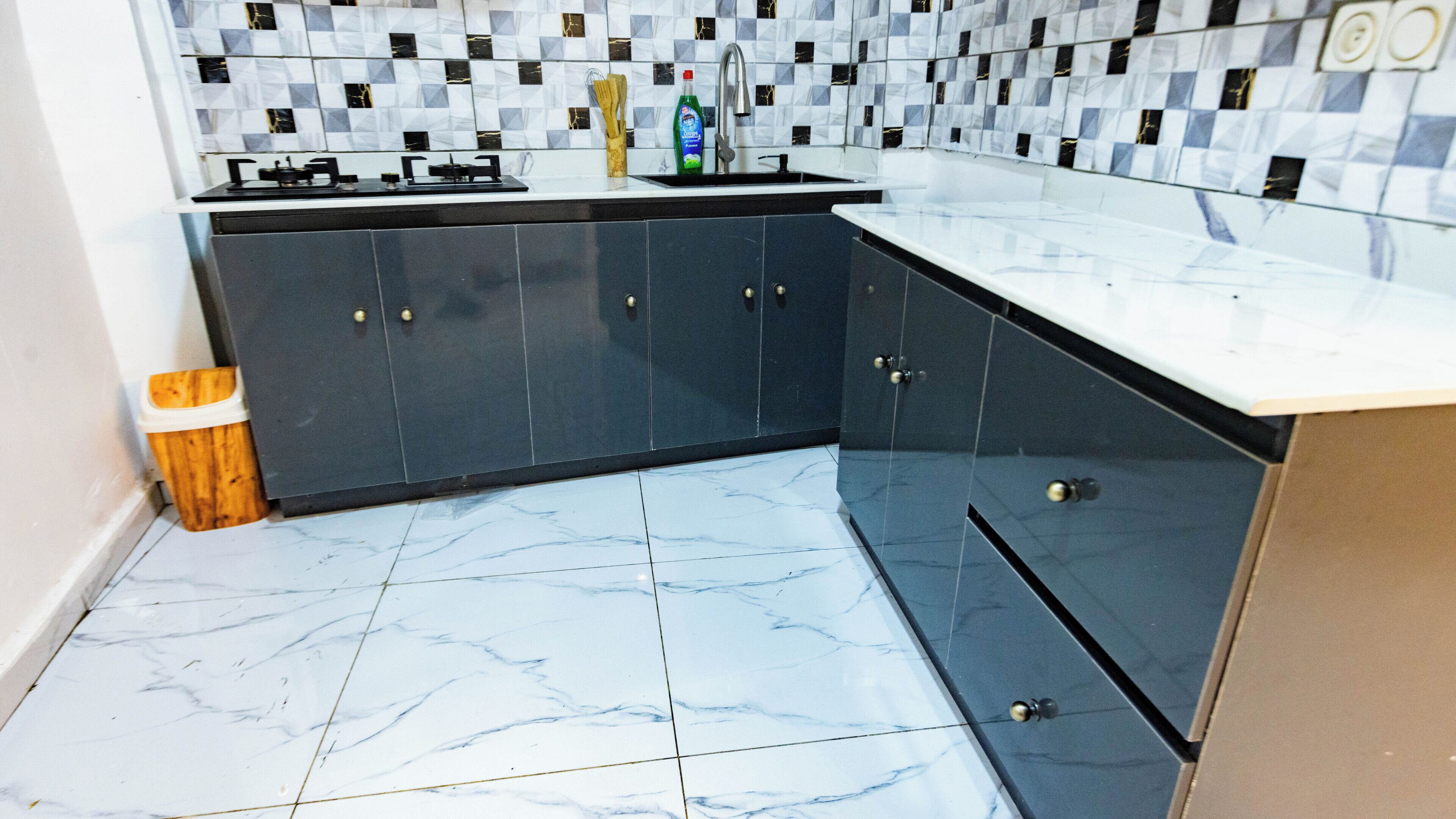 A kitchen with dark cabinets, a white countertop, and a tiled backsplash.