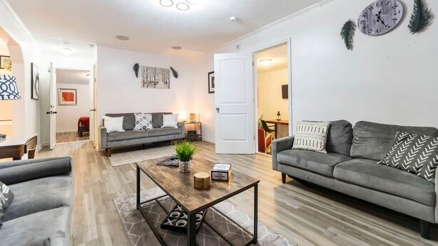 A modern living room with a grey sofa, a coffee table, and a dining area in the background.