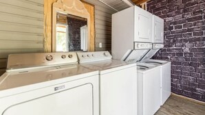 A laundry area with a Maytag washer and dryer, a wooden-framed mirror, and a brick wall.