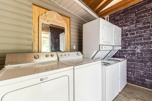 A laundry area with a Maytag washer and dryer, a wooden-framed mirror, and a brick wall.