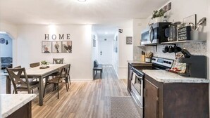 A modern kitchen with a built-in stove, microwave, and coffee station. There is a dining area with a wooden table and chairs.
