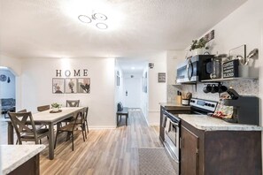 A modern kitchen with a built-in stove, microwave, and coffee station. There is a dining area with a wooden table and chairs.