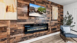 A modern living room with a wooden wall panel, a fireplace, a TV mounted above it, and a seating area with a chair.