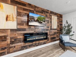 A modern living room with a wooden wall panel, a fireplace, a TV mounted above it, and a seating area with a chair.