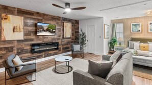 A modern living room with a fireplace, a ceiling fan, and a television mounted on the wall.
