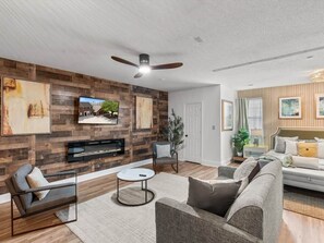 A modern living room with a fireplace, a ceiling fan, and a television mounted on the wall.