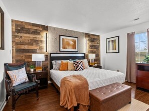 A bedroom with a bed, a chair, a nightstand, a lamp, and a window.