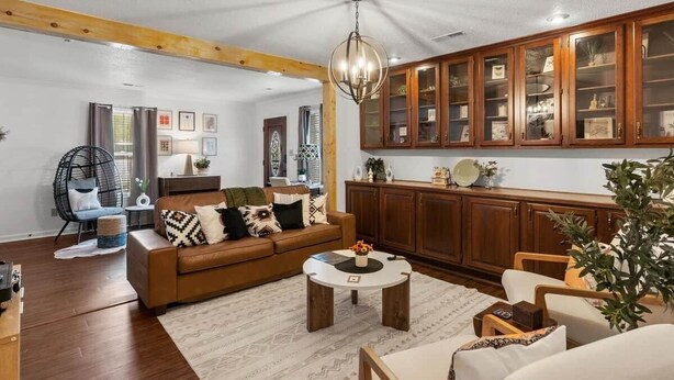 A living room with a brown sofa, a round coffee table, wooden cabinets, and a hanging light fixture.