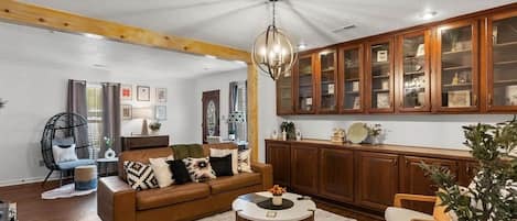 Una sala de estar con un sofá marrón, una mesa de centro redonda, armarios de madera y un colgador de luz.