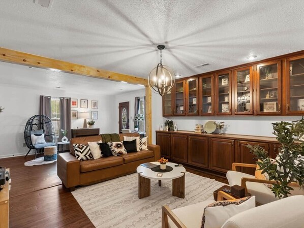 A living room with a brown sofa, a round coffee table, wooden cabinets, and a hanging light fixture.