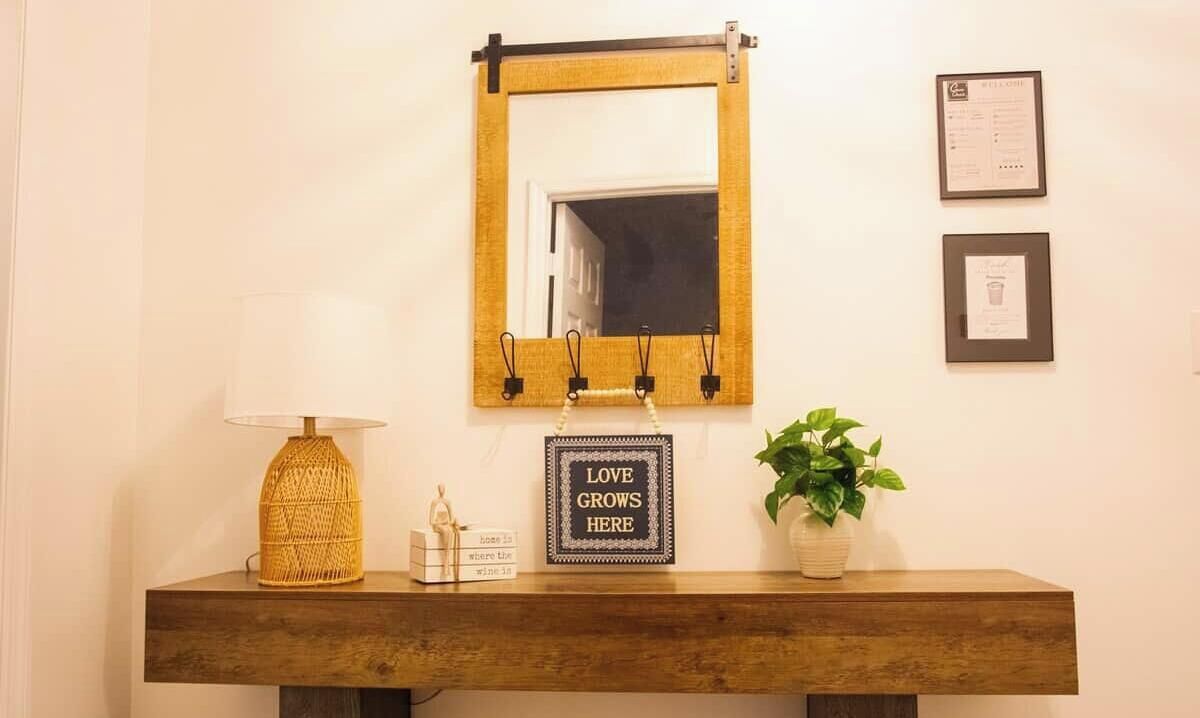 A wooden console table with a lamp, a framed sign, and a potted plant.