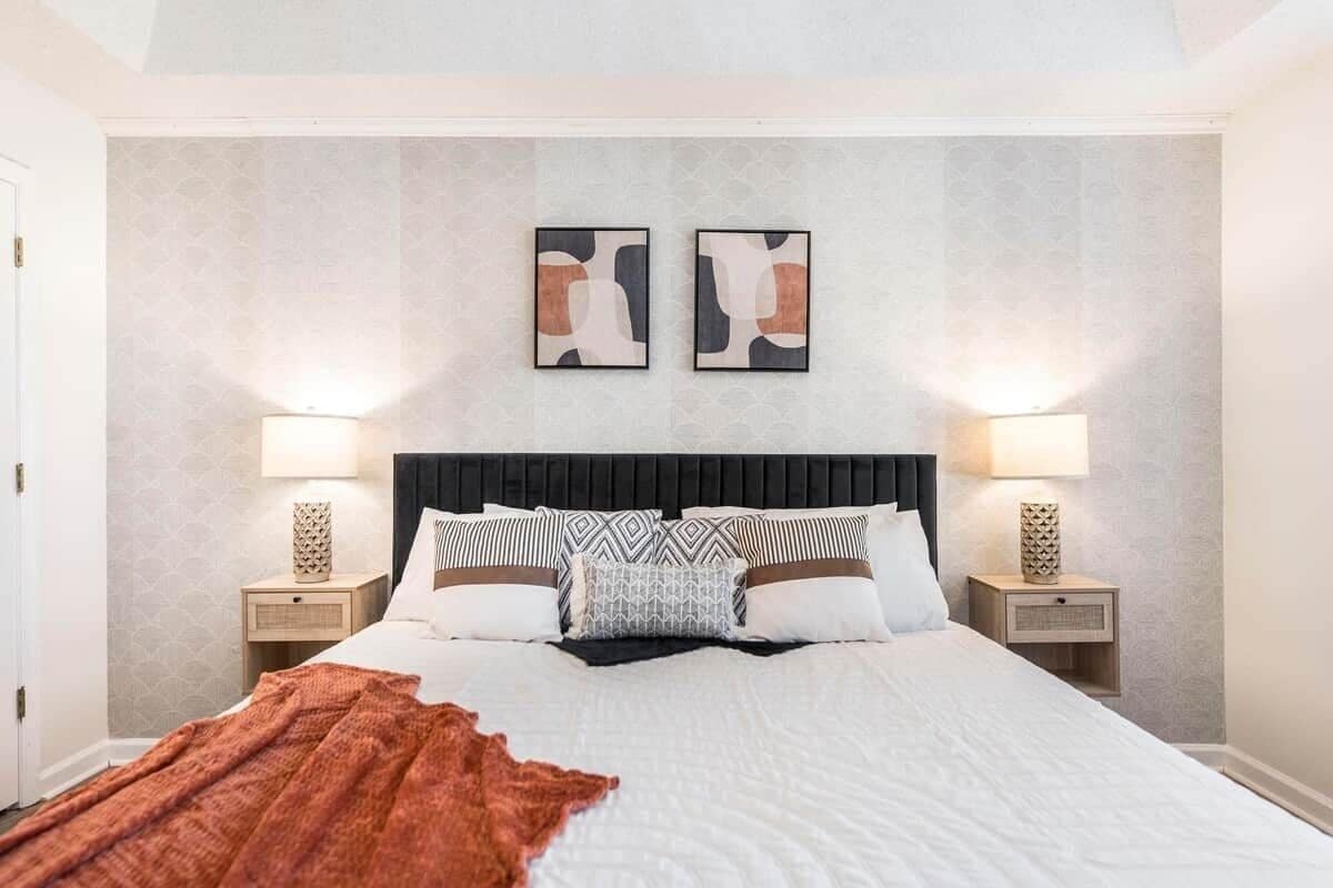 A neatly made bed with a black headboard, two bedside lamps, and two framed abstract artworks on the wall.