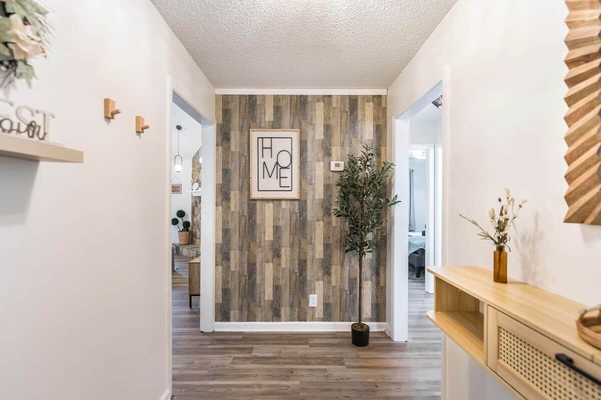 Un couloir avec un mur en bois, un panneau décoratif représentant le mot « MAISON », une plante en pot et une console en bois.