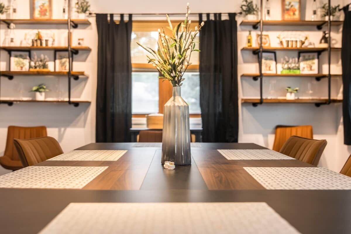 A conference room with a long table, two chairs on each side, a vase with flowers, and shelves with various items.