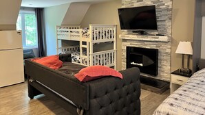 Een slaapkamer met stapelbedden, een open haard, een televisie en een bed met een rode kussen.