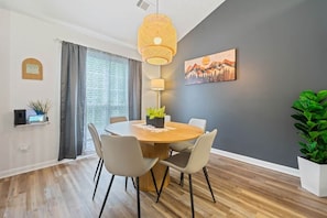 A dining area with a round table, chairs, a hanging light fixture, a wall-mounted lamp, a painting, and a potted plant. - Urban CasaOasis 5BR4BA Retreat Theatre & Game (Gwinnett County)